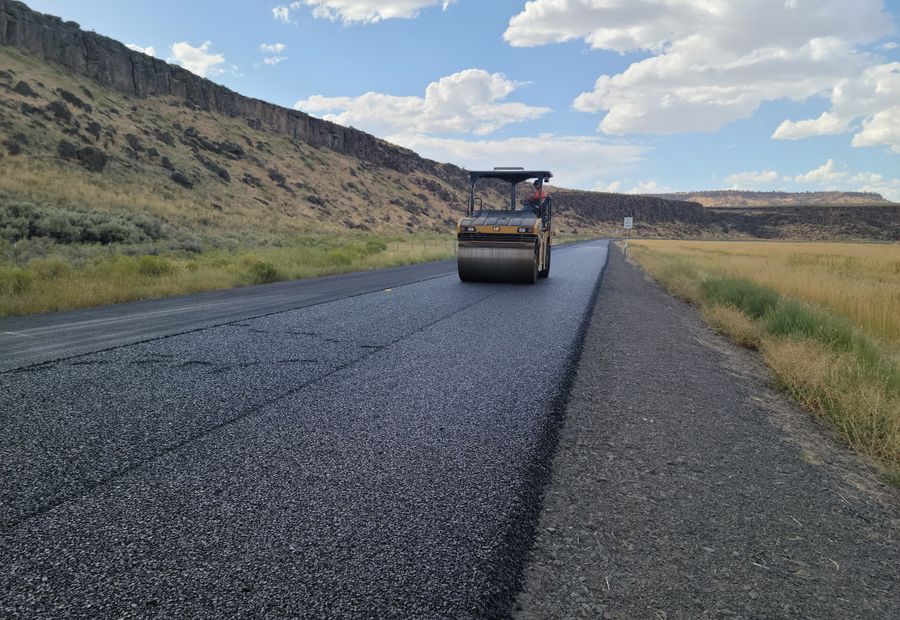 Double drum roller compacting a new asphalt surface course behind the paver