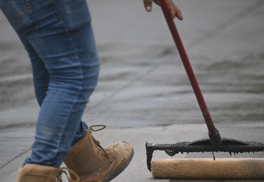 Worker pulling a squeegee of black sealer across a residential asphalt driveway
